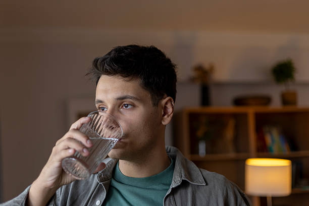 istock Young man drinking fresh water from a glass, staying hydrated and refreshed indoors 2239334865