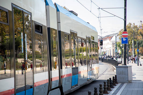 Modern trams moving along city street tracks in an urban environment. The photos show red and blue trams traveling through a European city during daylight. Tram rails curve along the road with trees, buildings, and street infrastructure visible in the background. The images depict urban public transportation, city infrastructure, and modern mobility systems. The environment appears clean and well-organized, capturing everyday traffic and transportation flow in a metropolitan area.