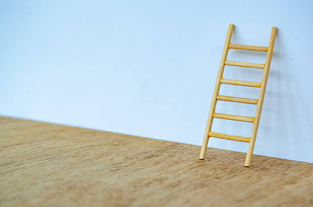 istock Wooden ladder standing tall against a white cover with customizable space for text or ideas. 2239344347
