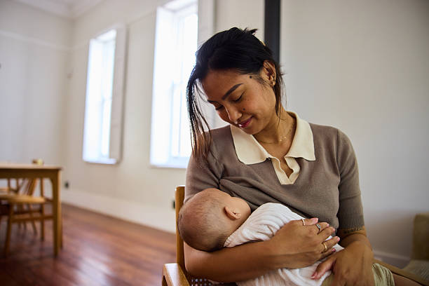 istock Young mom looking down at her baby while breastfeeding the child in softly lit dining area at home 2239349952