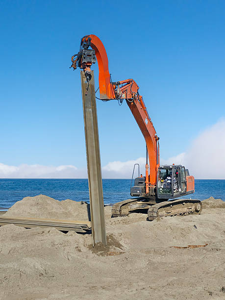 Pipe communications and city renovation. Upgrading infrastructure: yellow grader on construction site near river. Communication tower in the river on sky background in Downtown of Newport News, Virginia