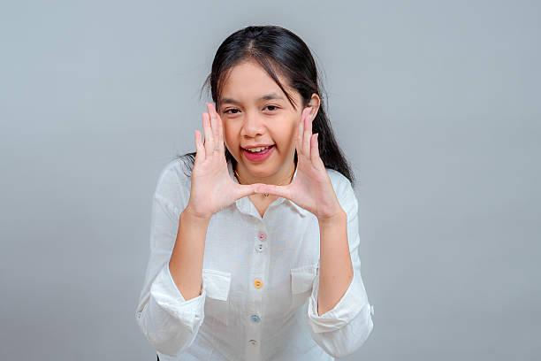 istock Cheerful young Asian woman making a shouting gesture with both hands, smiling playfully and expressing enthusiasm, excitement, and communication in a studio portrait setting. 2239353917