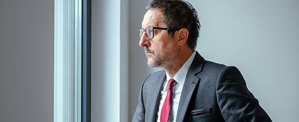 istock Concerned executive in formal attire gazing through office window, reflecting on challenges. 2239356846