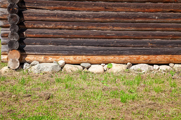 Close-up of a wooden log house built on a rubble stone foundation, showing details of log construction and foundation stones.