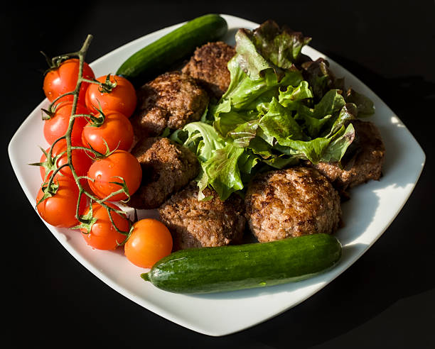 Fried Minced Meatballs with Cucumbers, Cherry Tomatoes and Lettuce on White Plate and Black Background
