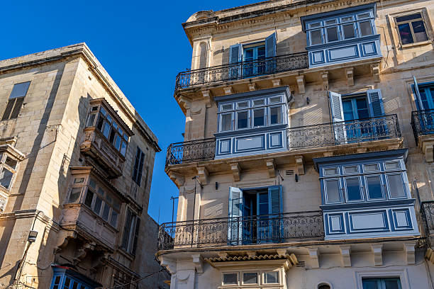Traditional painted wooden balconies and ornate wrought iron railings decorate sunlit Mediterranean limestone buildings.