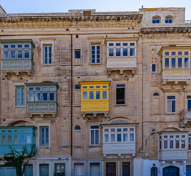 Historic building in Malta featuring stonework and a variety of pastel-colored wooden enclosed balconies.