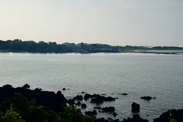 Basalt rocks fringe a calm bay on Jeju's northeast coast with low villages across the water near Hado Beach.