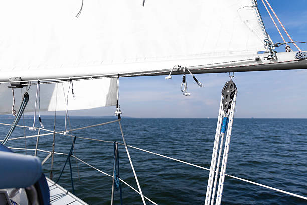 A close view along a sailboat's deck shows ropes, pulleys, and a white sail against a calm blue sea. Ideal for nautical, travel, and adventure themes in bright daylight.