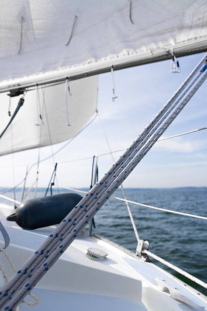 A close-up view of sailing ropes and rigging on a deck, with sails, blue water, and clear sky in the background, conveying freedom, adventure, and nautical ambiance.