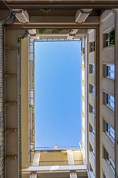 istock Symmetrical Courtyard View Looking Up at Blue Sky. Vertical upward view from an inner courtyard framed by classical apartment architecture, balconies, and vivid clear blue sky above. 2239382168