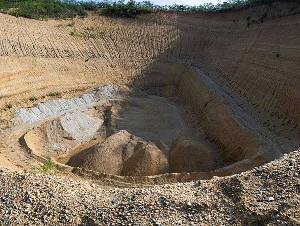 An abandoned sand quarry showcasing steep, layered geological formations. The exposed sediment layers and surrounding vegetation reveal the natural beauty and texture of the eroded landscape.