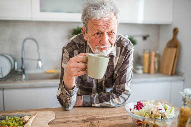 istock Smiling senior man standing leaning on kitchen counter drinking tea 2239383856