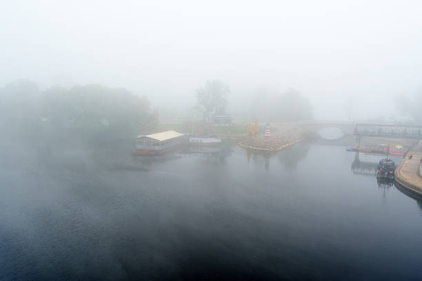An atmospheric horizontal shot of a modern concrete bridge reflected in the still water of a river on a dense, misty morning. The image conveys calm, nature, and a sense of connection.