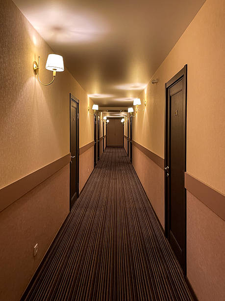 istock Long, empty hotel corridor stretching into the distance with warm wall sconce lighting and numerous closed doors, evoking a sense of travel and hospitality 2239389580