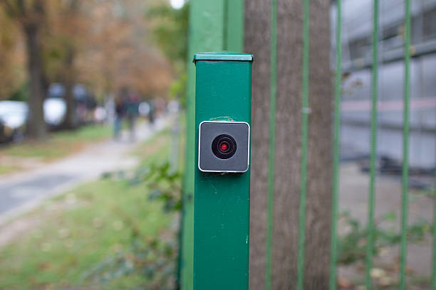 istock Surveillance camera mounted on a green pole in a tree-lined park setting during a cloudy day 2239396973
