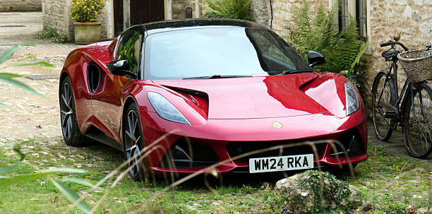 Castle Combe, United Kingdom - Sept 17 2025 A red lotus Emira sports car is parked beside an old bicycle in a village in the Cotswolds