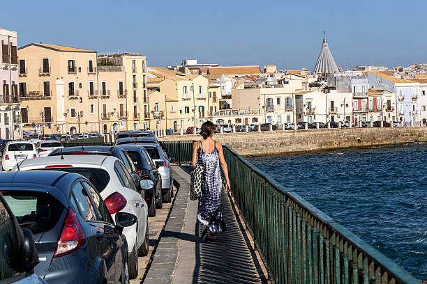 Young woman walking along Syracuse sunny waterfront. Syracuse, Italy - October 3, 2025