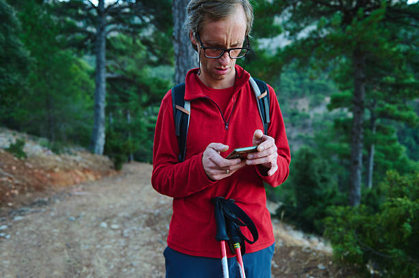 istock Hiker In Red Jacket Using Smartphone On Forest Trail With Trekking Poles 2239401019