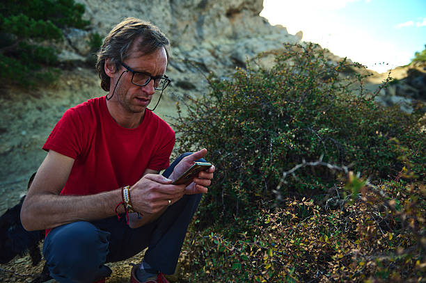 istock Man in Red Shirt Using Smartphone Outdoors Among Rocks and Bushes 2239401091