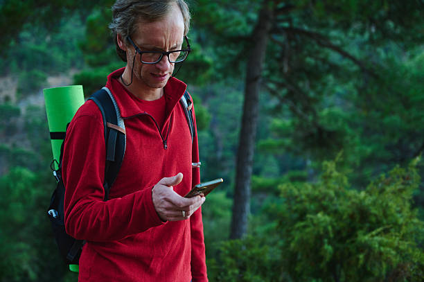 Hiker With Red Fleece Jacket Checking Smartphone On Forest Trail, Wearing Backpack With Green Sleeping Mat, Ready For Outdoor Adventure