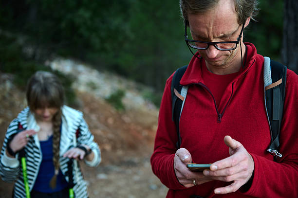 istock Hiking Duo Outdoors: Man in Red Jacket Using Smartphone While Woman Prepares Gear in Forest 2239401170