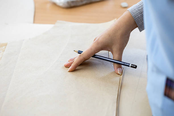 istock A fashion designer, cutter, or dressmaker working with paper sewing patterns on a large table. A concept of the creative process and handmade clothing design. 2239402526