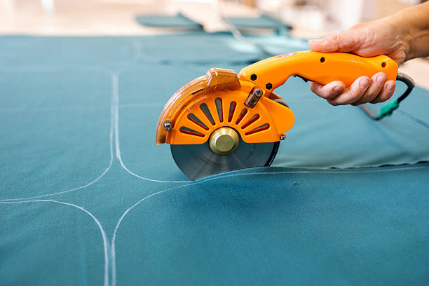 A cutter or pattern cutter uses an electric rotary cutter to cut through a stack of fabric in a garment factory. A concept of the textile industry and mass production.
