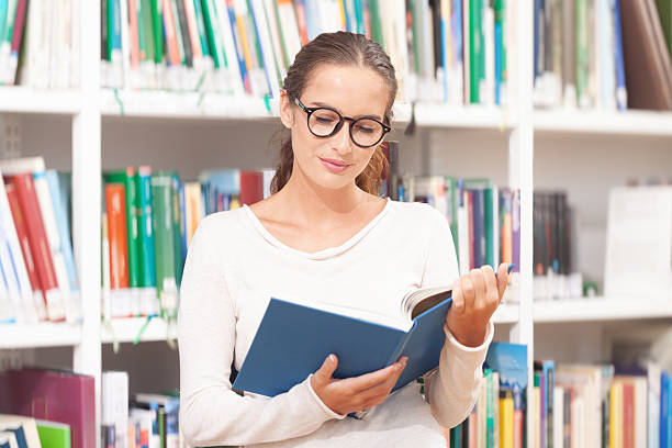 istock Young woman reading a book in a modern library 2239405024