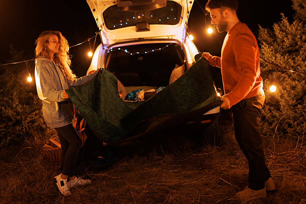 istock Couple preparing a camping setup in the dark with string lights and blankets near their car under a starry sky during a cozy outdoor evening 2239405100