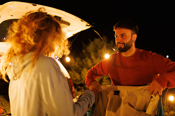 istock Couple enjoys a starry night while preparing for a camping trip in a forested area with warm lights illuminating the surroundings 2239405127
