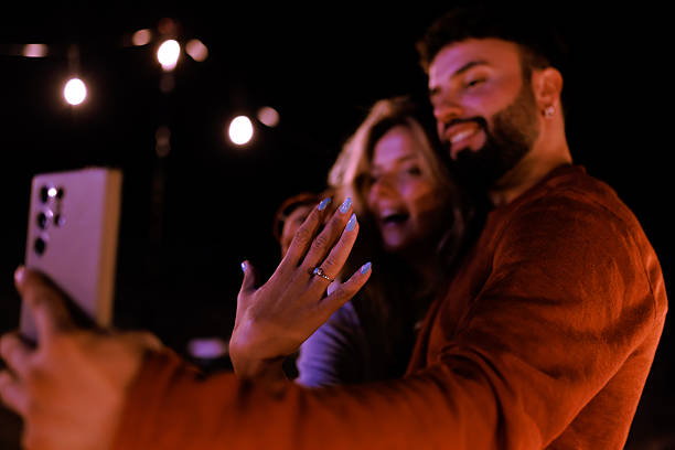 istock Couple joyfully takes a selfie while showing off an engagement ring at night celebration under string lights 2239405143