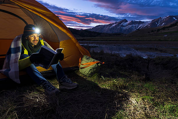 Hiker in the tent reading a book at dusk