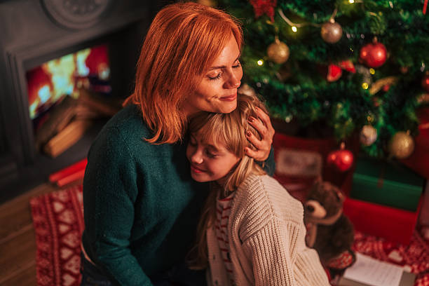 istock Mother daughter hugging by christmas tree and fireplace 2239411125