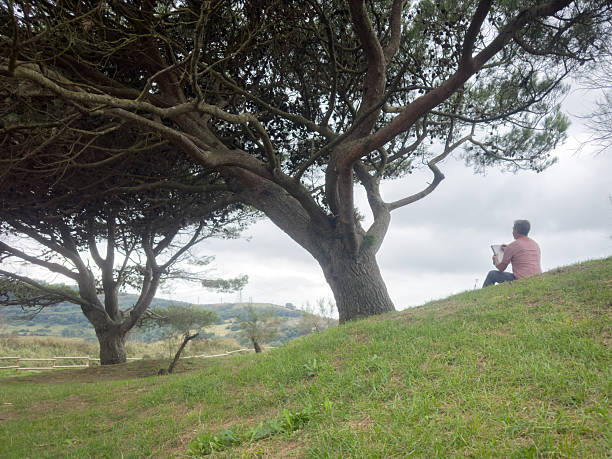 Man sitting on a grassy hillside, sketching the natural landscape and finding inspiration
