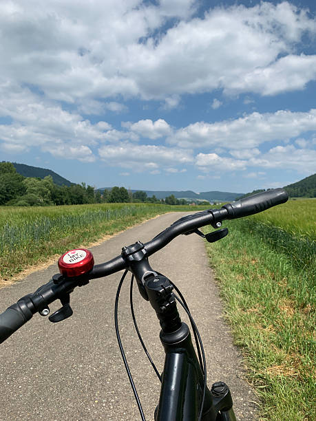 istock A cyclist rides along a peaceful path with lush green fields and beautiful clouds, enjoying a sunny day in the countryside 2239417495