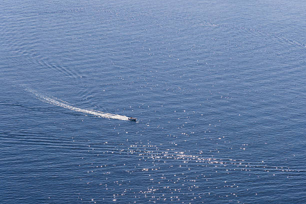 A lone small boat travels across a sunlit blue ocean, carving a bright wake. Calm water and glistening reflections evoke a sense of freedom, movement, and serenity on the water.