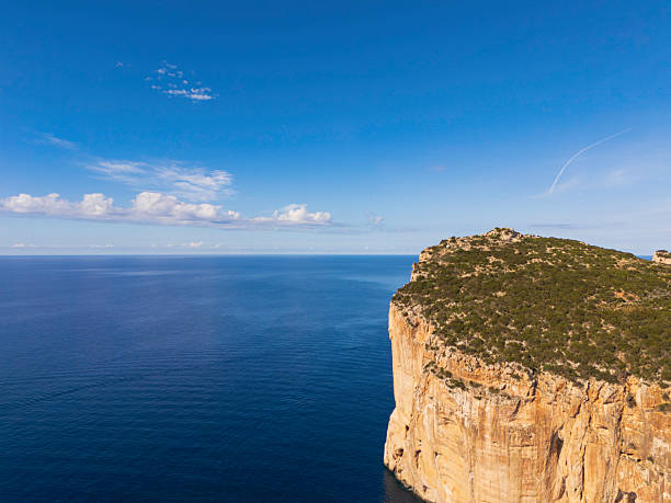 A dramatic cliff rises from the sea, covered in scrub, with a vast blue ocean and bright sky above. Ideal for travel, nature, and outdoor exploration themes.