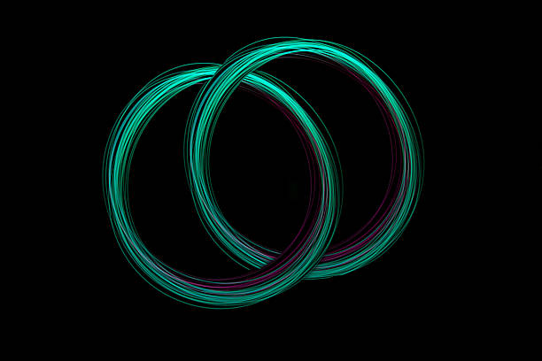 Bright light circles intertwine in an artistic display, showcasing flowing lines and vibrant colors in a dark setting.