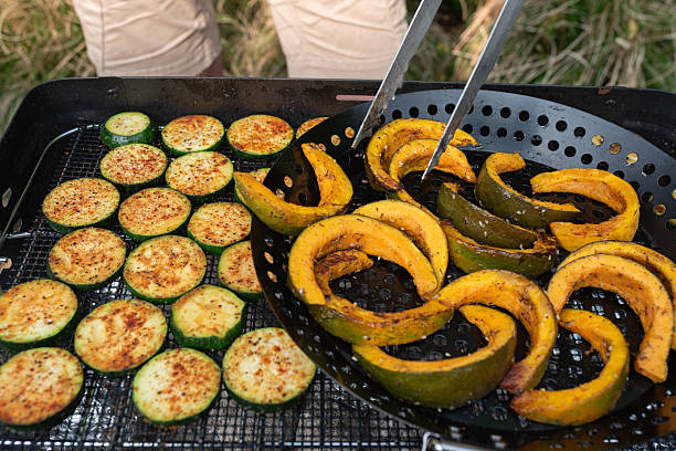 Close-up of freshly grilled zucchini and pumpkin slices being turned on an outdoor barbecue.