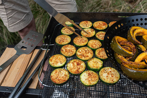 Close-up of zucchini slices and pumpkin wedges being grilled on a barbecue during a summer cookout.