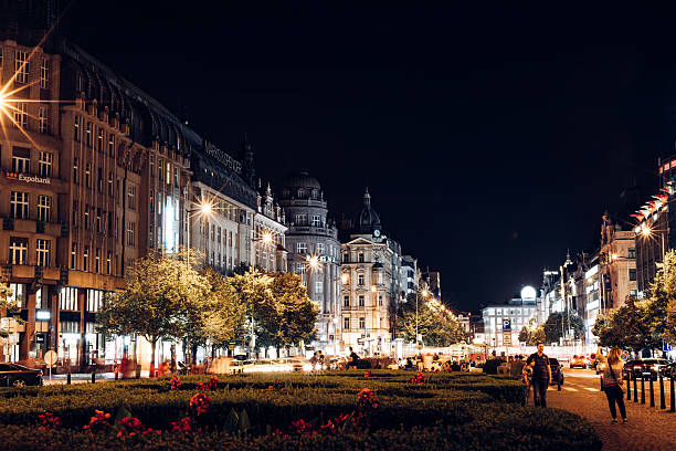 Pedestrians walking through Wenceslas Square in Prague at night.