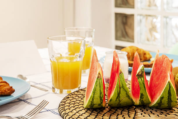 A dining table with breakfast set with lots of fruit, fresh orange juice and a white tablecloth
