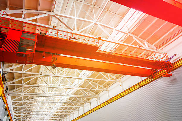 Overhead crane. Large Red Crane Operates in Spacious Industrial Warehouse During Bright Daylight. Gantry crane. Gantry crane with hook for lifting, moving heavy cargo. Granularity, blurred focus.