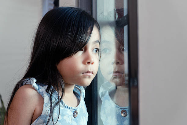 istock Little girl feeling sad looking out a window 2239440868