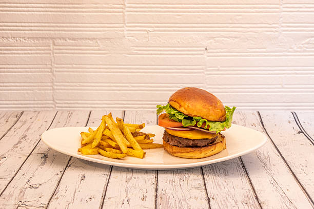 istock Classic beef burger with red onion, tomato slices, cheddar cheese and iceberg lettuce on a white tray and a side of French fries 2239441872