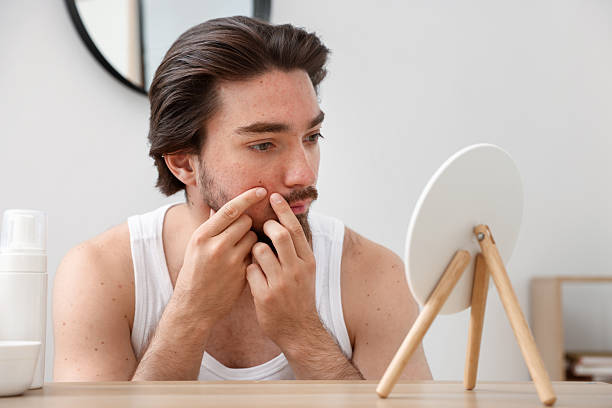 istock Young man with acne problem looking at mirror at table indoors 2239443366