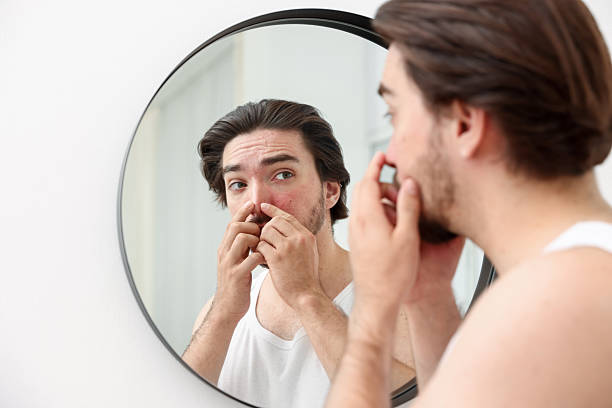 istock Young man with acne problem near mirror at home 2239443370