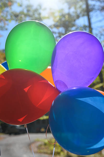 Close-up of four colorful balloons in mid-air against white background.