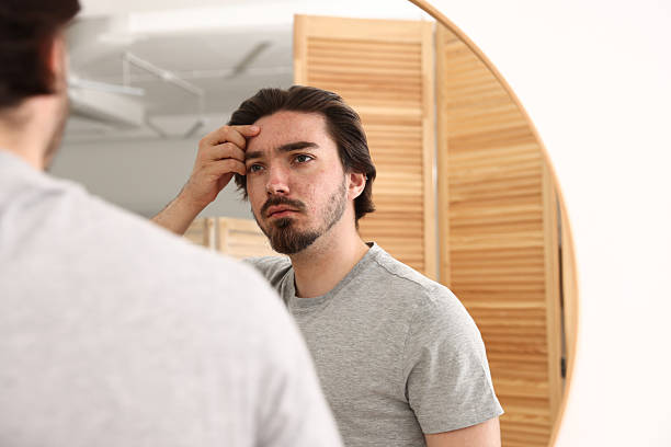 istock Young man with acne problem near mirror at home 2239444172